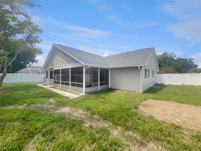 rear view of house with stucco siding, a gate, a fenced backyard, a yard, and a sunroom