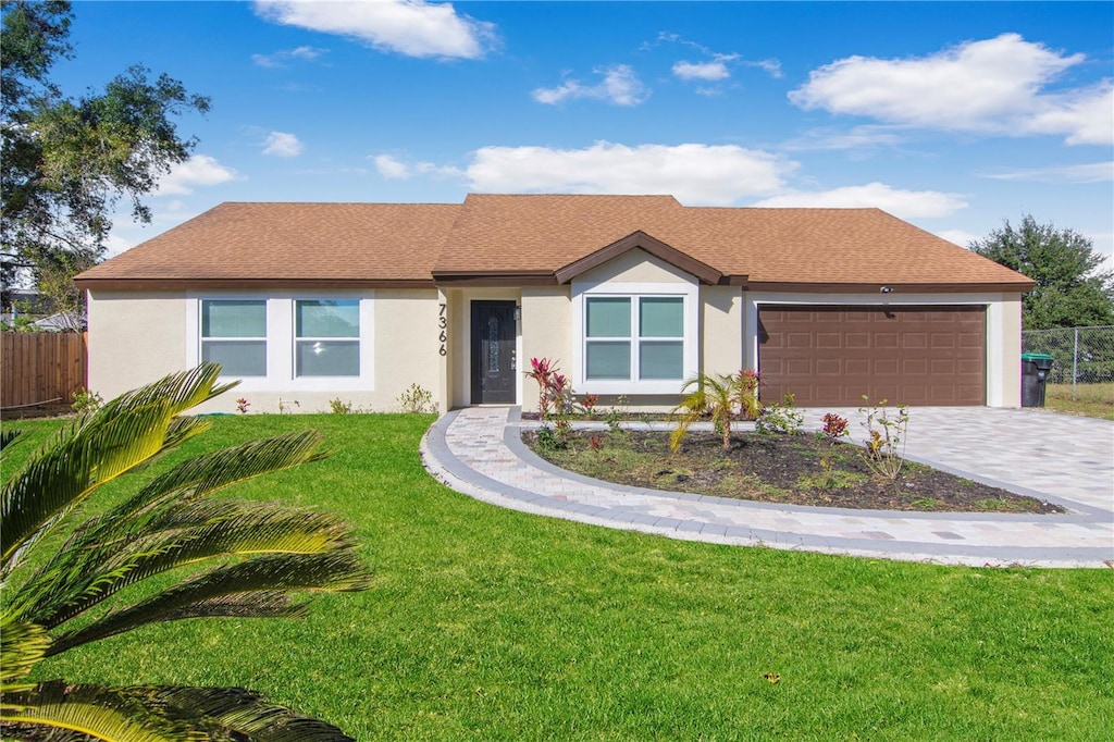 ranch-style home featuring stucco siding, a front lawn, decorative driveway, fence, and a garage