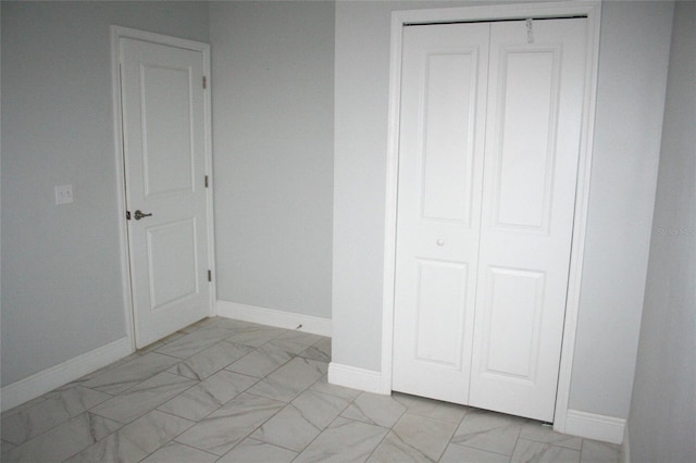 unfurnished bedroom featuring a closet, marble finish floor, and baseboards