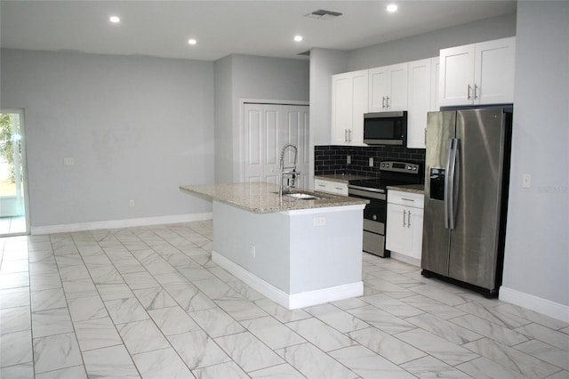 kitchen with light stone countertops, appliances with stainless steel finishes, a kitchen island with sink, sink, and white cabinetry