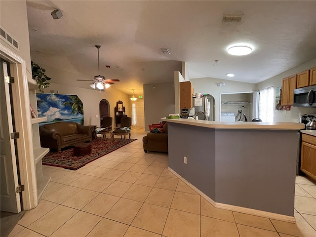 kitchen featuring a textured ceiling, light tile patterned floors, stainless steel appliances, ceiling fan, and vaulted ceiling