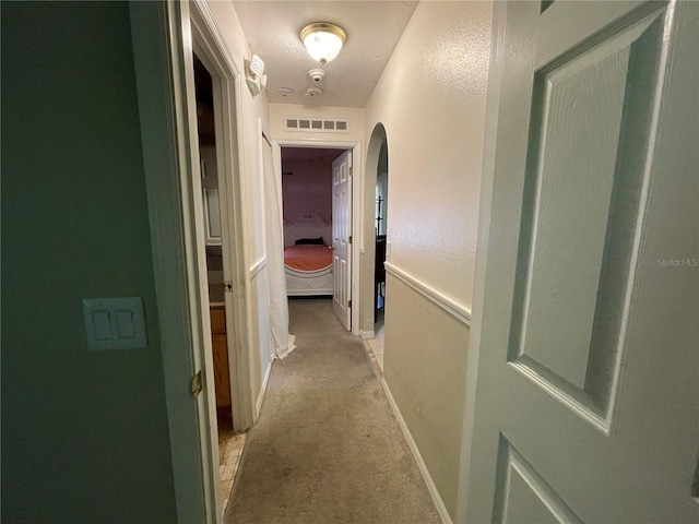 hall featuring light carpet, arched walkways, visible vents, and baseboards