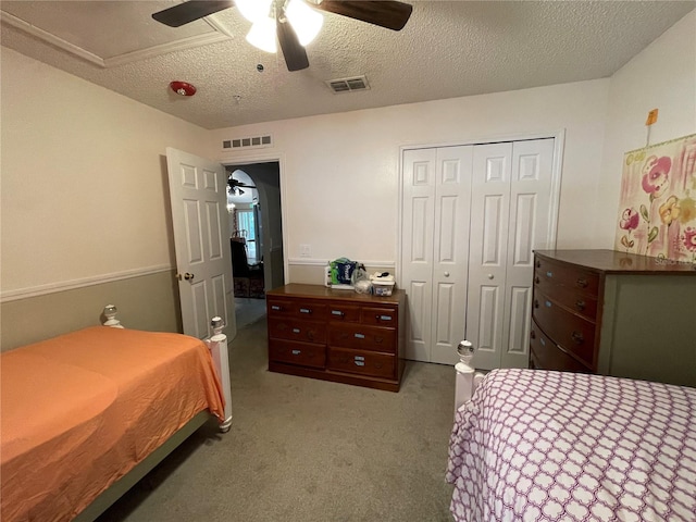 carpeted bedroom featuring a ceiling fan, a textured ceiling, visible vents, and a closet