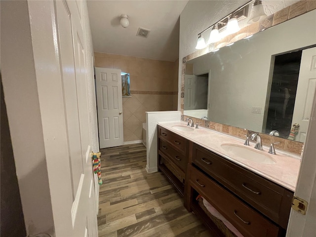 bathroom featuring wood finished floors, a sink, visible vents, tile walls, and double vanity