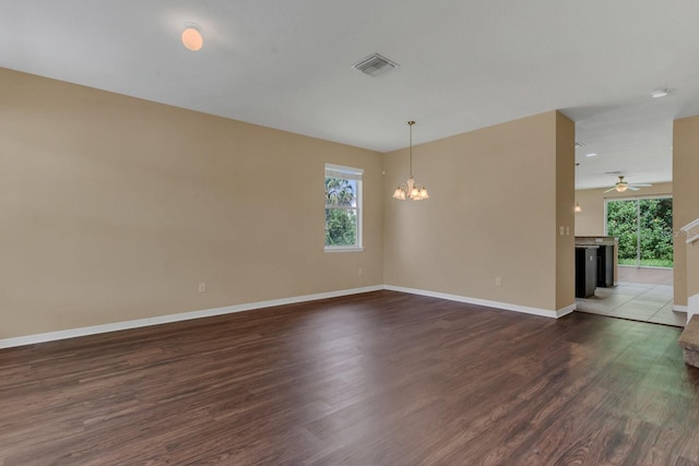 empty room with ceiling fan with notable chandelier, dark wood-type flooring, baseboards, and visible vents