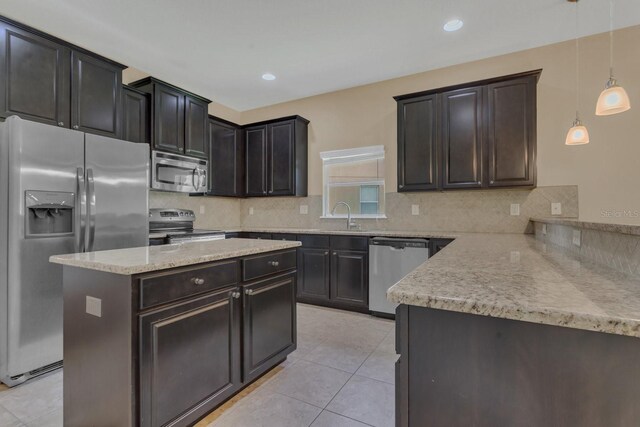 kitchen featuring pendant lighting, tasteful backsplash, stainless steel appliances, a kitchen island, and light stone countertops