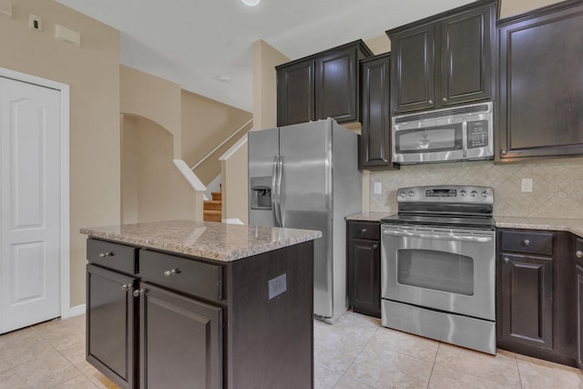 kitchen with backsplash, light tile patterned floors, a center island, light stone counters, and stainless steel appliances