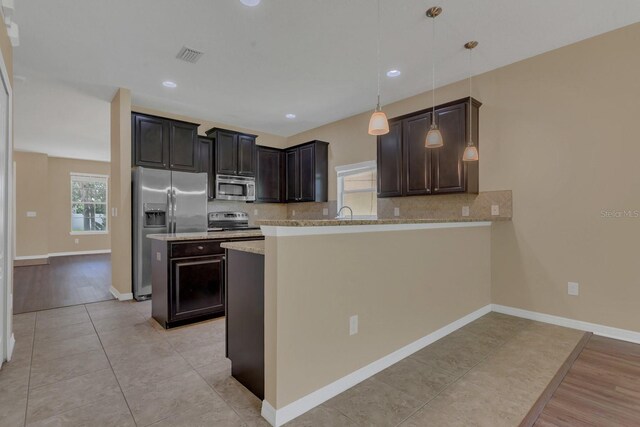 kitchen with pendant lighting, light hardwood / wood-style flooring, stainless steel appliances, kitchen peninsula, and light stone counters