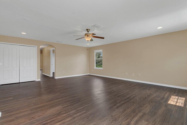 spare room with dark wood-type flooring, baseboards, arched walkways, and ceiling fan