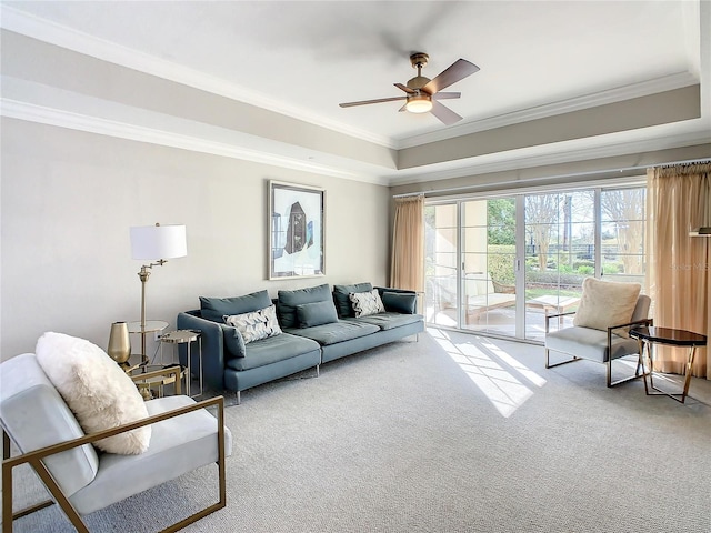 living area with a raised ceiling, carpet, ceiling fan, and crown molding