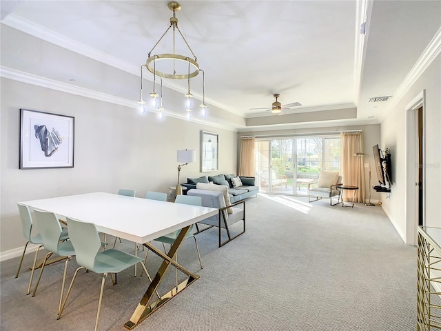 dining space with ceiling fan, crown molding, a raised ceiling, and light carpet