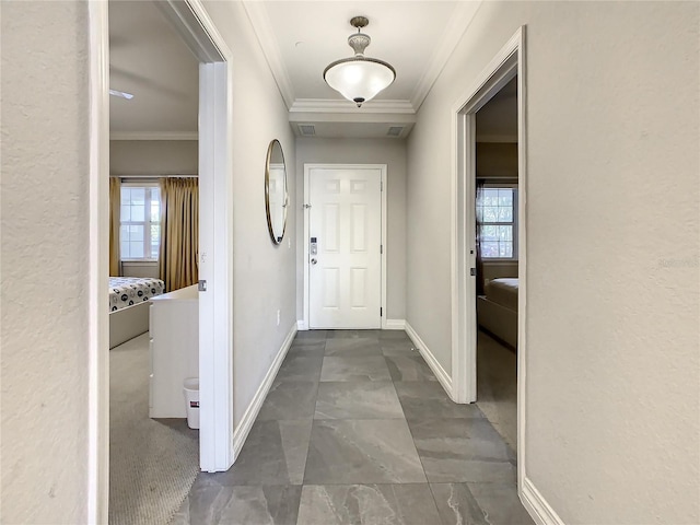 hallway with visible vents, baseboards, a healthy amount of sunlight, and ornamental molding