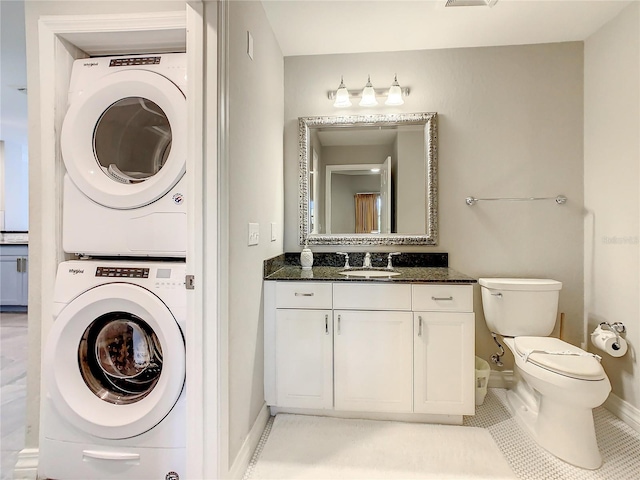 bathroom with toilet, tile patterned flooring, stacked washer / dryer, baseboards, and vanity