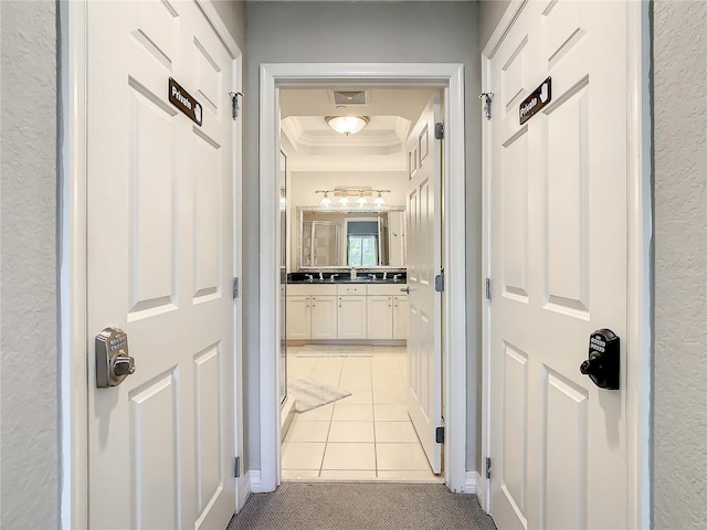 hallway featuring light tile patterned flooring, ornamental molding, light carpet, a raised ceiling, and a textured wall