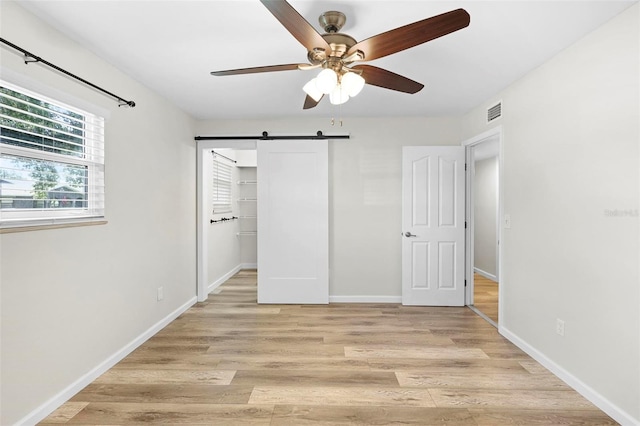 unfurnished bedroom with light wood-type flooring, ceiling fan, a barn door, and a closet