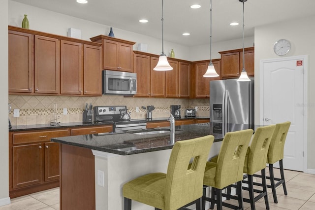 kitchen with appliances with stainless steel finishes, a kitchen bar, hanging light fixtures, and a center island with sink