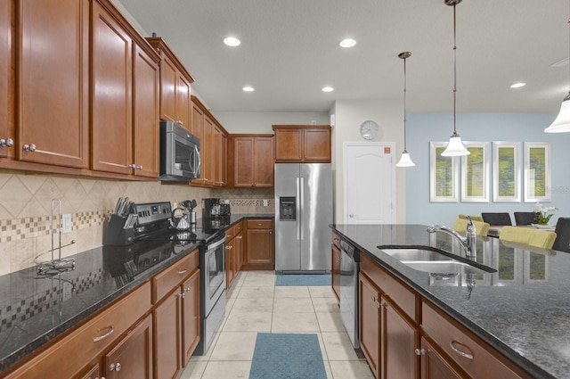 kitchen with dark stone countertops, light tile patterned floors, sink, hanging light fixtures, and appliances with stainless steel finishes