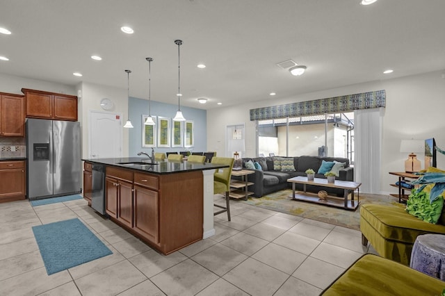 kitchen with a kitchen breakfast bar, stainless steel fridge, decorative light fixtures, a center island with sink, and dishwasher