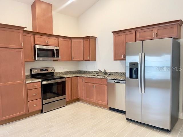 kitchen with high vaulted ceiling, appliances with stainless steel finishes, light stone counters, and sink