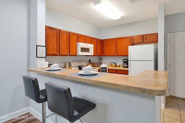 kitchen with white appliances, kitchen peninsula, light tile patterned floors, and a kitchen breakfast bar