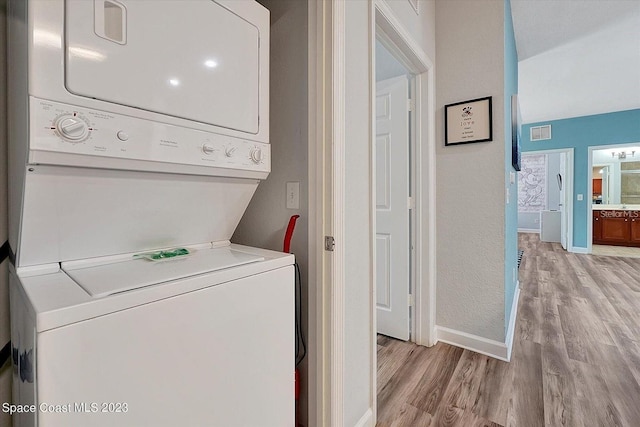 clothes washing area with stacked washing maching and dryer and light hardwood / wood-style floors