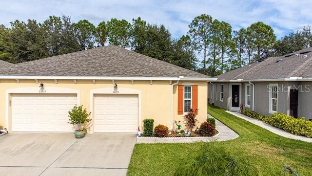 view of front of property with a shingled roof, concrete driveway, stucco siding, an attached garage, and a front yard