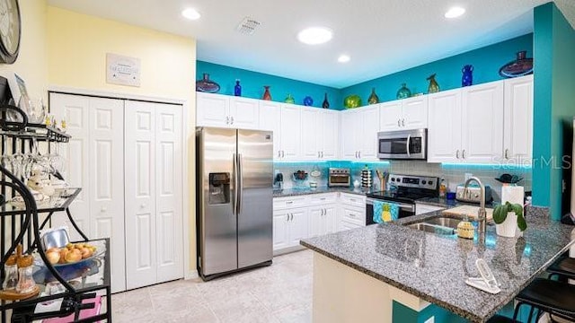 kitchen featuring stainless steel appliances, white cabinetry, a sink, dark stone countertops, and a peninsula