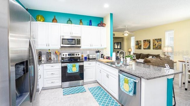 kitchen featuring appliances with stainless steel finishes, open floor plan, white cabinets, a sink, and a peninsula