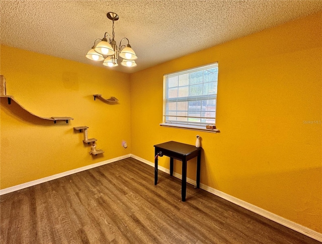 empty room featuring a textured ceiling, an inviting chandelier, and dark hardwood / wood-style flooring