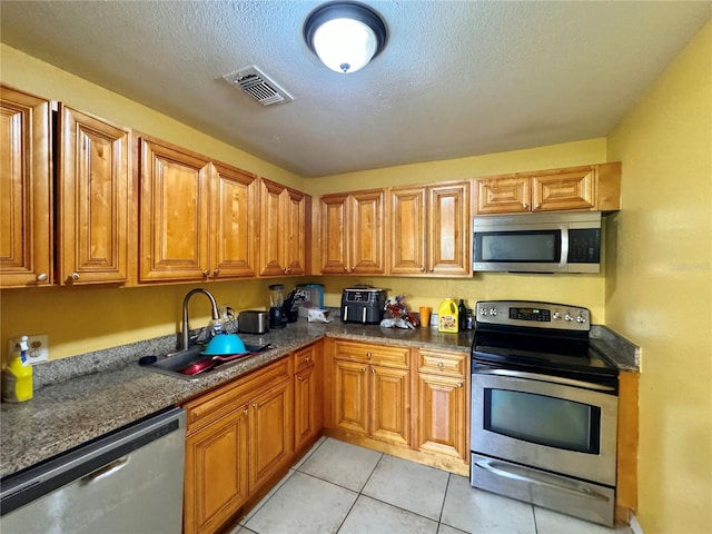 kitchen with dark stone countertops, stainless steel appliances, sink, light tile patterned flooring, and a textured ceiling