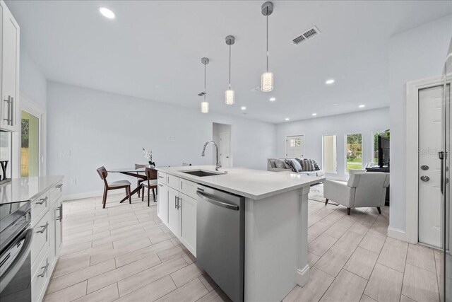 kitchen with white cabinets, stainless steel appliances, sink, pendant lighting, and a center island with sink