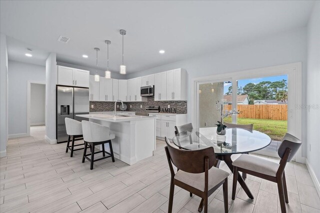 kitchen featuring hanging light fixtures, appliances with stainless steel finishes, white cabinetry, sink, and a kitchen island with sink