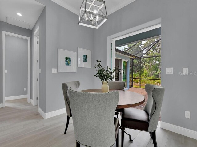 dining room featuring light wood-type flooring, lofted ceiling, a notable chandelier, and ornamental molding