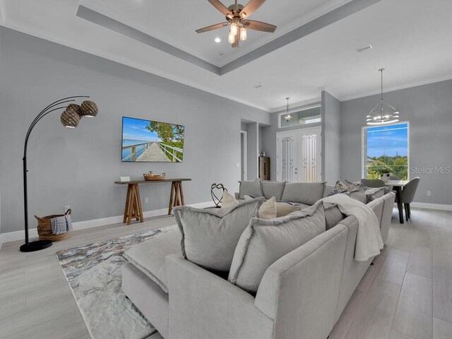 living room with ceiling fan with notable chandelier, ornamental molding, a tray ceiling, and light hardwood / wood-style floors