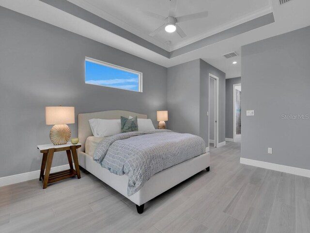 bedroom featuring ceiling fan, ornamental molding, light wood-type flooring, and a tray ceiling