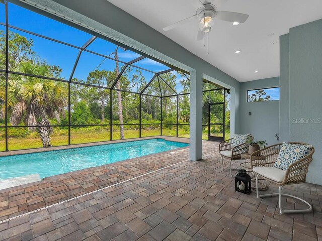 view of swimming pool with glass enclosure, ceiling fan, and a patio