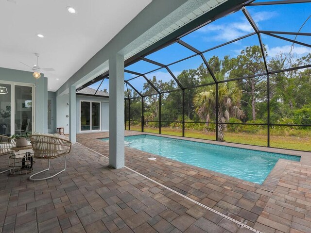 view of swimming pool with glass enclosure, ceiling fan, and a patio