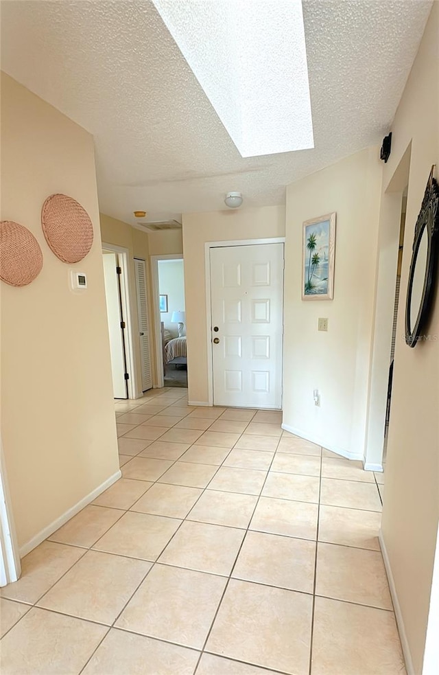 interior space with a skylight, a textured ceiling, and light tile patterned flooring