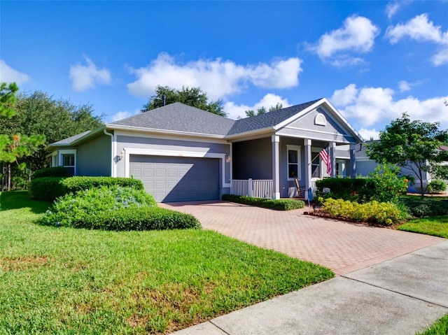 ranch-style home with a front yard, an attached garage, covered porch, stucco siding, and decorative driveway