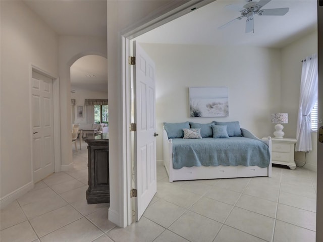 bedroom with light tile patterned floors, baseboards, arched walkways, and ceiling fan