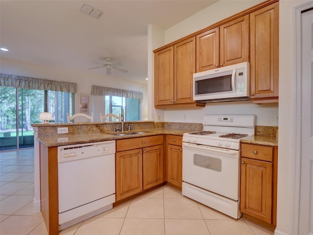 kitchen with light stone countertops, light tile patterned floors, a peninsula, white appliances, and a sink