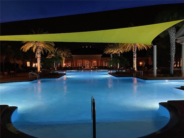 pool at night featuring a patio area and a community pool