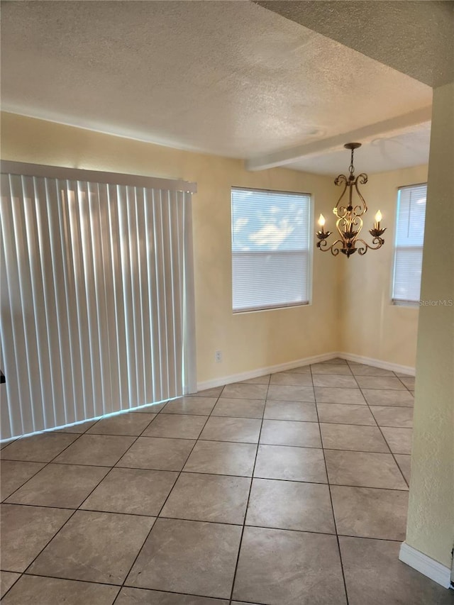 tiled spare room with beamed ceiling, a textured ceiling, and an inviting chandelier