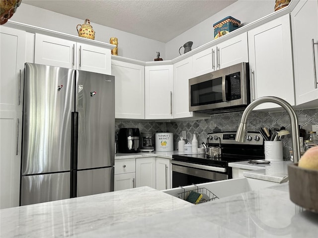 kitchen with appliances with stainless steel finishes, white cabinetry, tasteful backsplash, light stone countertops, and a textured ceiling