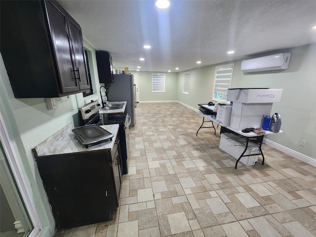 kitchen with stainless steel appliances, light countertops, a wall mounted AC, dark cabinetry, and baseboards