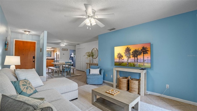 living room featuring a textured ceiling, light tile patterned floors, and ceiling fan