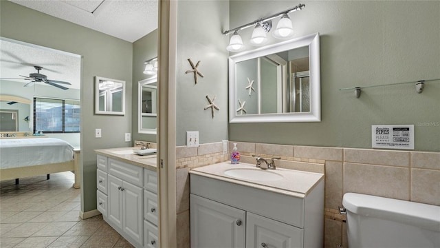 bathroom with vanity, tile patterned flooring, tile walls, toilet, and ceiling fan