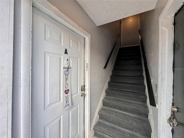 stairway with a textured ceiling and wood finished floors