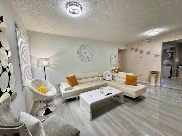 living area with a textured ceiling, wood finished floors, visible vents, and baseboards