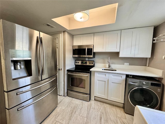 kitchen with stainless steel appliances, a sink, visible vents, white cabinets, and washer / clothes dryer